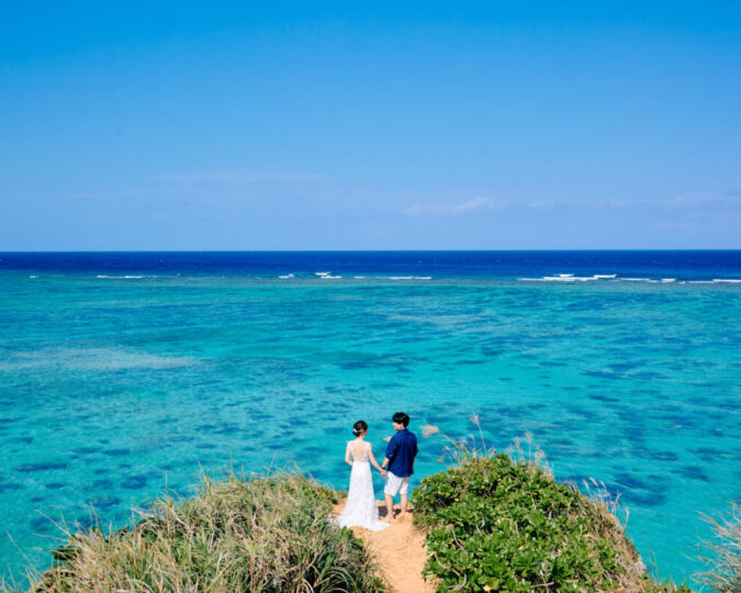 エメラルドグリーンの海を見下ろす高台に立つ新郎新婦