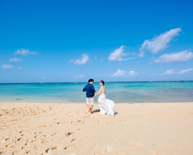 青い海と白い砂浜を歩くウェディングドレスの新婦と新郎